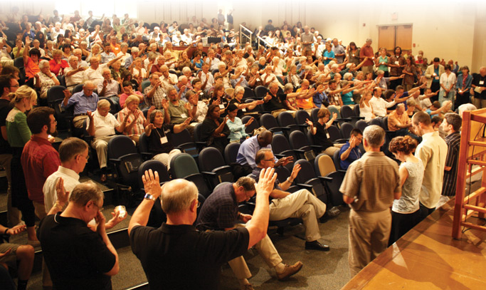 Participants reach out in a prayer of blessing for those commissioned for service Friday evening. Photo: Jon Trotter