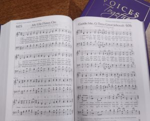 New Voices Together hymnal with purple cover. Book open to page 605 My Life Flown On and page 606 Guide Men, O Thou Great jehovah